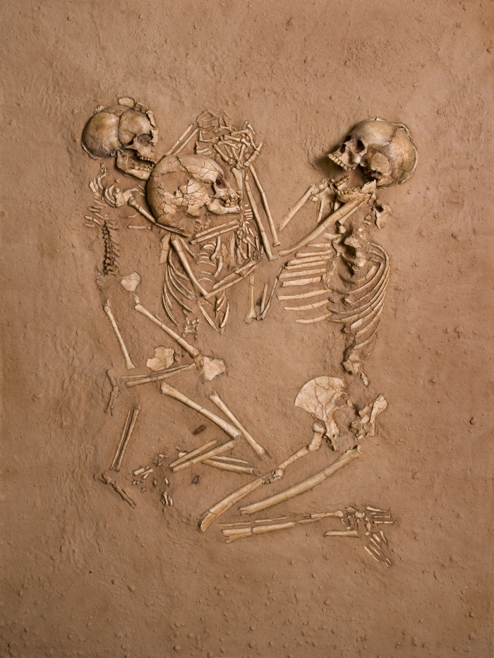 
	Triple Burial at Gobero
	Mike Hettwer ©2008 National Geographic

	Figure Caption: The skeletons and artifacts of the exceptional triple burial at Gobero are preserved in this cast exactly as found by Paul Sereno, Explorer-in-Residence at the National Geographic Society. Pollen clusters found underneath the skeletons indicate the bodies had been laid atop flowers, and the burial also contained four arrowheads. The people died without any sign of skeletal injury.
	
	The final substantial human occupation of Gobero is called the Tenerean occupation. Humid conditions returned to the region, and the lake refilled. Radiocarbon and OSL dates indicate that Gobero was occupied between about 5200 and 2500 BC.
	
	Burials in the Tenerean occupation are more varied than in the Kiffian period, with some tightly bound burials, some recumbent, and some, like this multiple burial of a woman and two children, intertwined with others. Physical analysis of the skeletal material make it clear that this is a different population from the earlier Kiffians, although some of the artifacts are similar.
	
	The Tenerean people at Gobero were probably partly semi-sedentary hunter-gatherer-fishers, with some amount of cattle herding. Pottery with stamped impressions, projectile points with deep basal notches, bracelets and pendants of hippo ivory, and pendants made of a fine-grained greenstone were discovered in association with Tenerean burials. Animal bones found include hippos, antelope, softshell turtles, crocodiles and a few domestic cattle. Pollen studies suggest that Gobero was a mosaic of shrubland and grasslands, with some tropical trees.
	
	After the end of the Tenerean period, Gobero was abandoned, except for some transient presence of nomadic cattle herders; the final desertification of the Sahara had started and Gobero could no longer support long-term habitation.
	Source: National Geographic