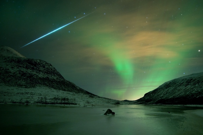 
	Aurora Shimmer, Meteor Flash
	Astronomy Picture of the Day - 2009 December 19
	Credit & Copyright: Bjørnar G. Hansen,
	
	Explanation: Northern Lights, or aurora borealis, haunted skies over the island of Kvaløya, near Tromsø Norway on December 13. This 30 second long exposure records their shimmering glow gently lighting the wintery coastal scene. A study in contrasts, it also captures the sudden flash of a fireball meteor from December's excellent Geminid meteor shower. Streaking past familiar stars in the handle of the Big Dipper, the trail points back toward the constellation Gemini, off the top of the view. Both aurora and meteors occur in Earth's upper atmosphere at altitudes of 100 kilometers or so, but aurora are caused by energetic charged particles from the magnetosphere, while meteors are trails of cosmic dust.