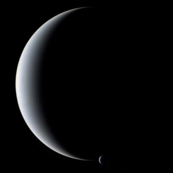 
	Crescent Neptune and Triton
	Astronomy Picture of the Day - 2009 December 13
	Credit: Voyager 2, NASA
	
	Explanation: Gliding silently through the outer Solar System, the Voyager 2 spacecraft camera captured Neptune and Triton together in crescent phase in 1989. The above picture of the gas giant planet and its cloudy moon was taken from behind just after closest approach. It could not have been taken from Earth because Neptune never shows a crescent phase to sunward Earth. The unusual vantage point also robs Neptune of its familiar blue hue, as sunlight seen from here is scattered forward, and so is reddened like the setting Sun. Neptune is smaller but more massive than Uranus, has several dark rings, and emits more light than it receives from the Sun.