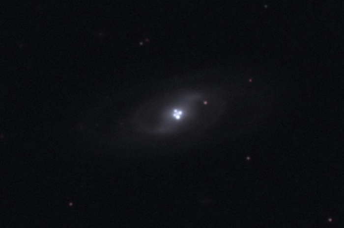 
	The Einstein Cross Gravitational Lens
	Credit & Copyright: J. Rhoads (ASU) et al., WIYN, AURA, NOAO, NSF
	Astronomy Picture of the Day - 2010 February 7
	
	Explanation: Most galaxies have a single nucleus -- does this galaxy have four? The strange answer leads astronomers to conclude that the nucleus of the surrounding galaxy is not even visible in this image. The central cloverleaf is rather light emitted from a background quasar. The gravitational field of the visible foreground galaxy breaks light from this distant quasar into four distinct images. The quasar must be properly aligned behind the center of a massive galaxy for a mirage like this to be evident. The general effect is known as gravitational lensing, and this specific case is known as the Einstein Cross. Stranger still, the images of the Einstein Cross vary in relative brightness, enhanced occasionally by the additional gravitational microlensing effect of specific stars in the foreground galaxy.