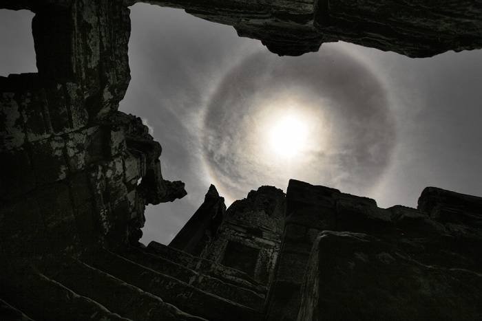 
	A Sun Halo Over Cambodia
	Credit & Copyright: Nagy Attila
	Astronomy Picture of the Day - 2010 February 8
	
	Explanation: Have you ever seen a halo around the Sun? This fairly common sight occurs when high thin clouds containing millions of tiny ice crystals cover much of the sky. Each ice crystal acts like a miniature lens. Because most of the crystals have a similar elongated hexagonal shape, light entering one crystal face and exiting through the opposing face refracts 22 degrees, which corresponds to the radius of the Sun halo. A similar Moon halo may be visible during the night. Pictured above, a nearly complete sun halo was photographed high above the ancient Bayon temple in Angkor, Cambodia. Exactly how ice-crystals form in clouds remains under investigation.