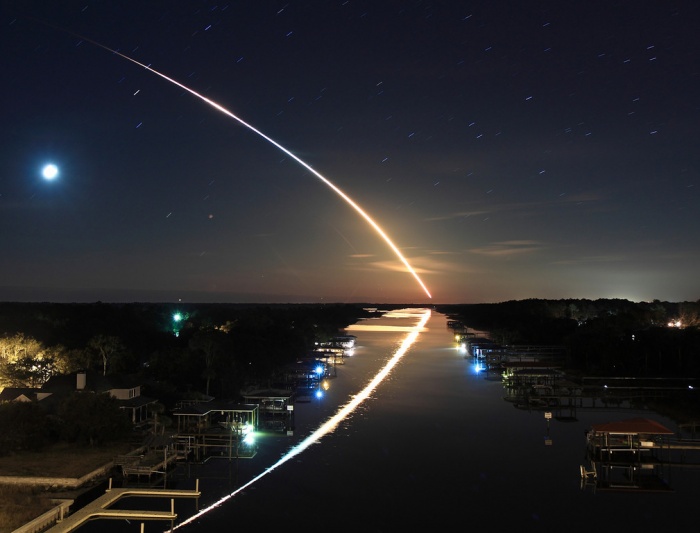 
	Waterway to Orbit
	Credit & Copyright: James Vernacotola
	Astronomy Picture of the Day - 2010 February 13
	
	Explanation: The 32nd shuttle mission to the International Space Station, STS-130, left planet Earth on February 8. Its early morning launch to orbit from Kennedy Space Center's pad 39A followed the long, graceful, eastward arc seen in this 2 minute time exposure. Well composed, the dramatic picture also shows the arc's watery reflection from the Intracoastal Waterway Bridge, in Ponte Vedra, Florida, about 115 miles north of the launch site. In the celestial background a waning crescent Moon and stars left their own short trails against the still dark sky. The brightest star trail near the moon was made by red supergiant Antares, alpha star of the constellation Scorpius.