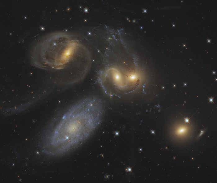    Stephan's Quintet  Credit:   Hubble Legacy Archive, ESA, NASA; Processing: Hunter Wilson Astronomy Picture of the Day - 2010 November 20  Explanation: The first identified compact galaxy group, Stephan's Quintet is featured in this eye-catching image constructed with data drawn from the extensive Hubble Legacy Archive. About 300 million light-years away, only four galaxies of the group are actually locked in a cosmic dance of repeated close encounters. The odd man out is easy to spot, though. The four interacting galaxies (NGC 7319, 7318A, 7318B, and 7317) have an overall yellowish cast and tend to have distorted loops and tails, grown under the influence of disruptive gravitational tides. But the larger bluish galaxy, NGC 7320, is much closer than the others. Just 40 million light-years distant, it isn't part of the interacting group. In fact, individual stars in the foreground galaxy can be seen in the sharp Hubble view, hinting that it is much closer than the others. Stephan's Quintet lies within the boundaries of the high flying constellation Pegasus.