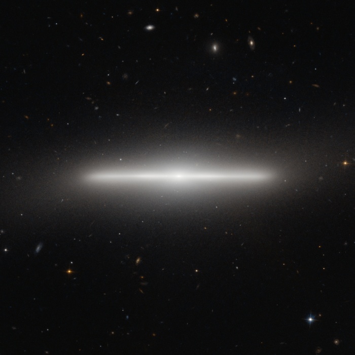    Multiverses: NGC 4452: An Extremely Thin Galaxy  Credit: ESA, Hubble, NAS   Astronomy Picture of the Day - 2010 November 9  Explanation: Why is there a line segment on the sky? In one of the more precise alignments known in the universe, what is pictured above is actually a disk galaxy being seen almost perfectly edge on. The image from the Hubble Space Telescope is a spectacular visual reminder of just how thin disk galaxies can be. NGC 4452, a galaxy in the nearby Virgo Cluster of Galaxies, is so thin that it is actually difficult to determine what type of disk galaxy it is. Its lack of a visible dust lane indicates that it is a low-dust lenticular galaxy, although it is still possible that a view from on top would reveal spiral structure. The unusual stellar line segment spans about 35,000 light years from end to end. Near NGC 4452's center is a slight bulge of stars, while hundreds of background galaxies are visible far in the distance. Galaxies that appear this thin are rare mostly because our Earth must reside (nearly) in the extrapolated planes of their thin galactic disks. Galaxies that actually are this thin are relatively common -- for example our own Milky Way Galaxy is thought to be about this thin.